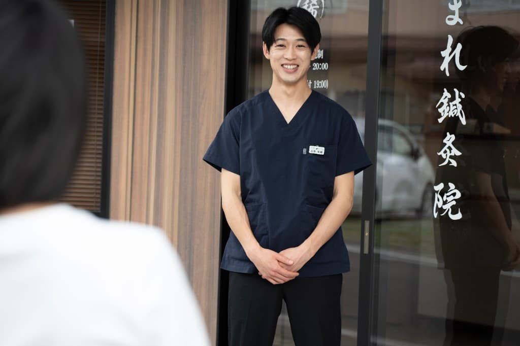 まれ鍼灸院の院長が院内入口で笑顔で迎える様子